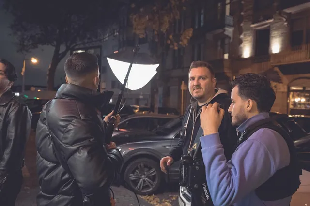 Camera operator in a Steadicam vest talking between parked cars